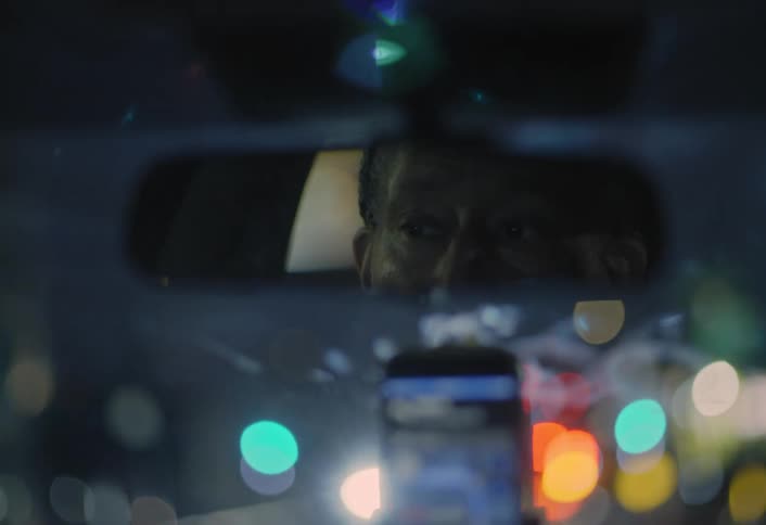 A man is driving a car down a road with his cellphone in a holder on the dashboard