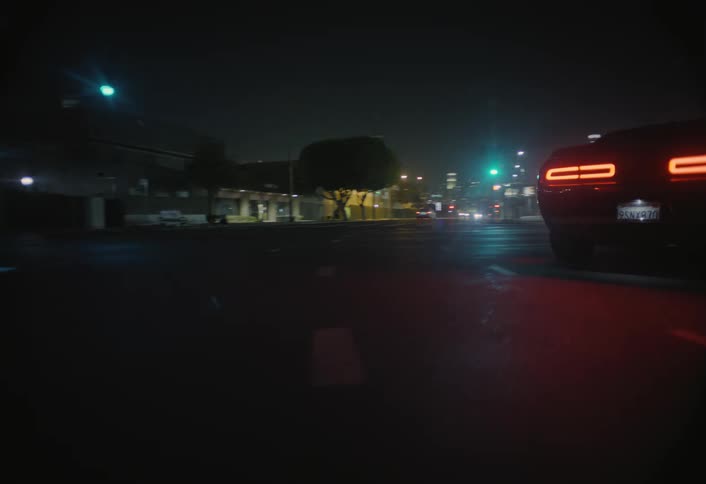 The glowing red taillights of a car are followed as it drives through a city at night