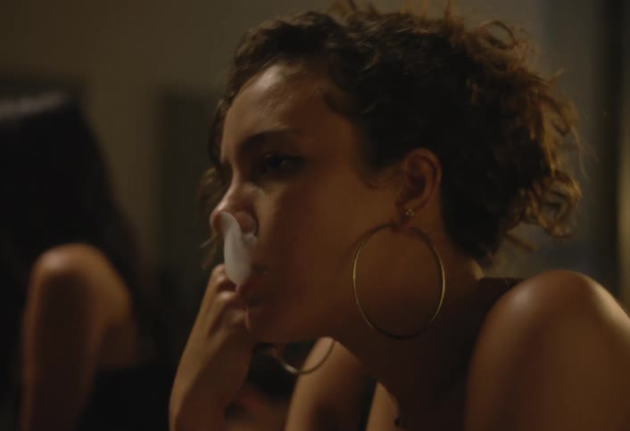 Teenager girl with a sad face expression smoking and holding a bottle on her hand surrounded by other people talking and walking indoors