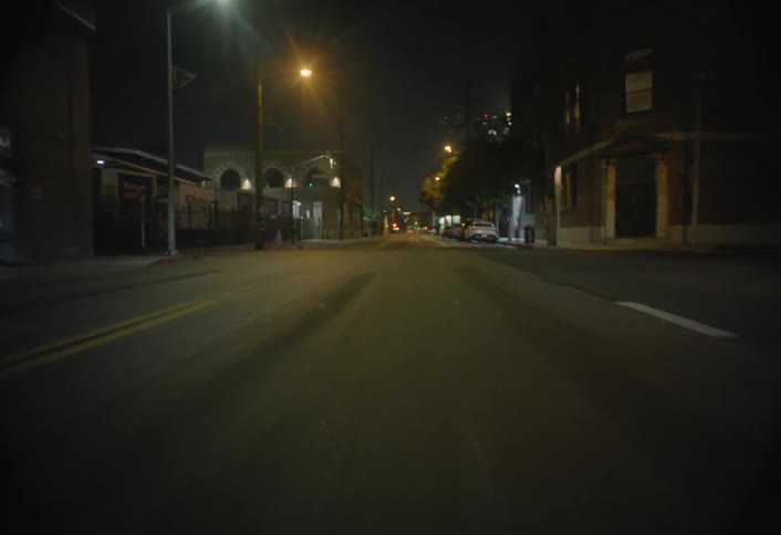 A car drives down an empty illuminated city street at night