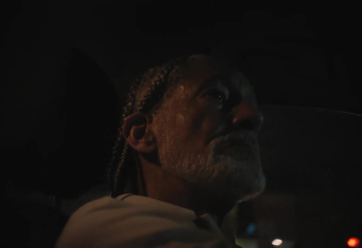 Man drives at night with a focused expression lit by external light