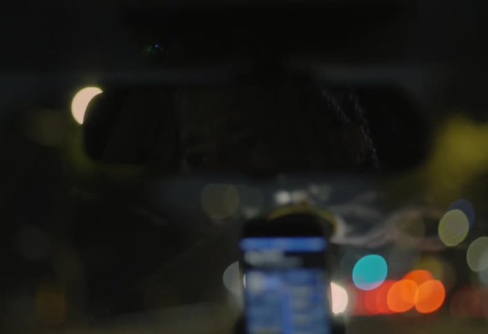 Rear view mirror reflects the driver as he drives through the city at night using a smartphone held in a hands free device