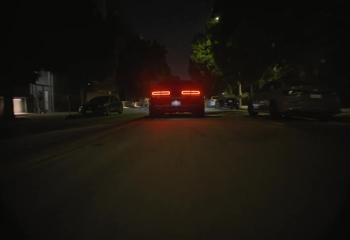 Car drives down an empty street at night with tail lights on