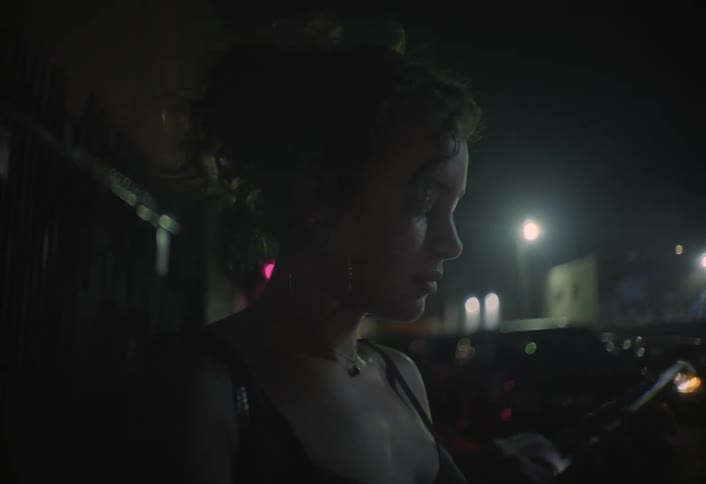 The woman uses her phone and smokes at night