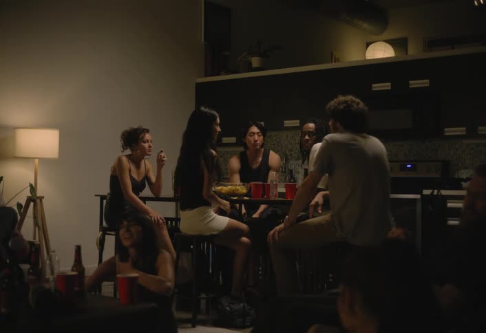 A group of young adults are seat around a table while drinking and conversing