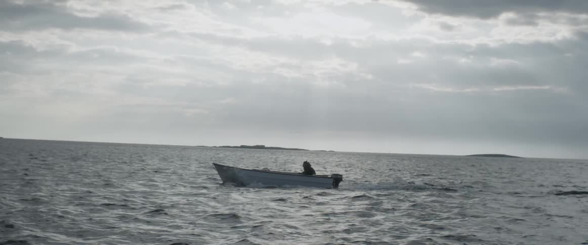 Small boat moving through a large body of water on a cloudy day