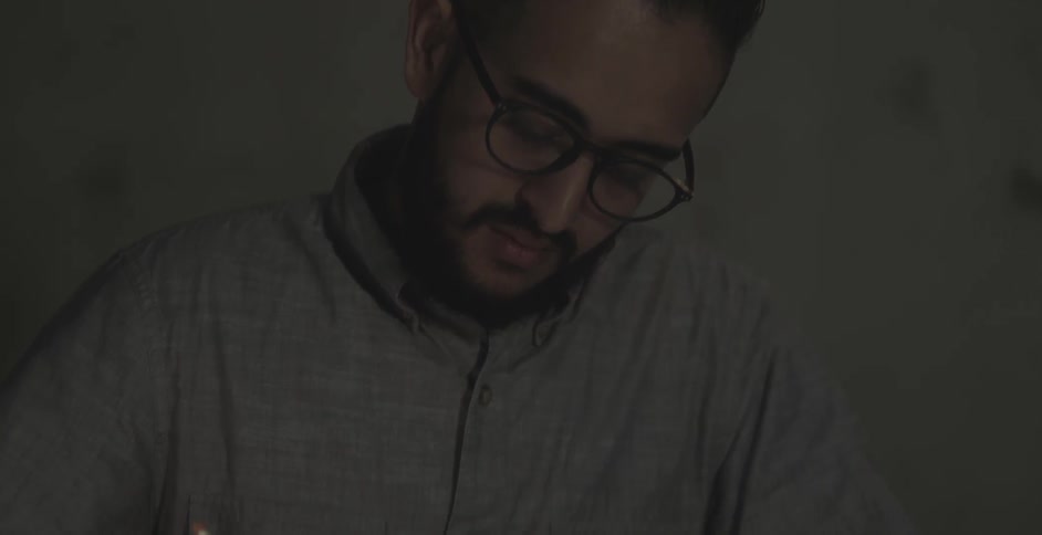 A man is writing at a desk in a dark office
