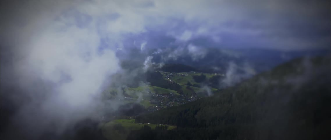 The view of a town located in a valley below is obscured by clouds