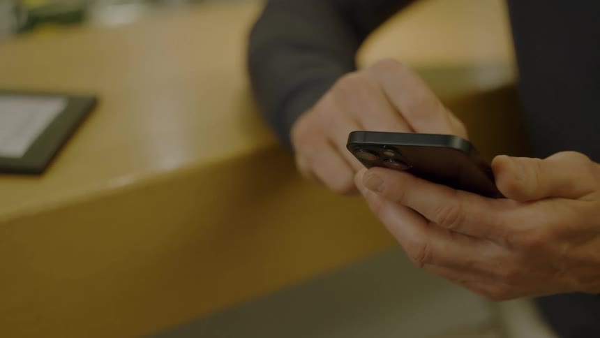 Person holds smartphone and types a message over a wooden counter