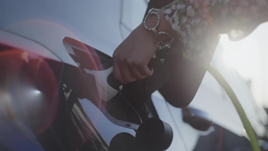 Close up of a young woman plugging in her electric vehicle to charge during daytime