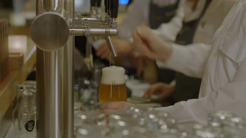 Person pours golden draft beer into a glass at a busy bar