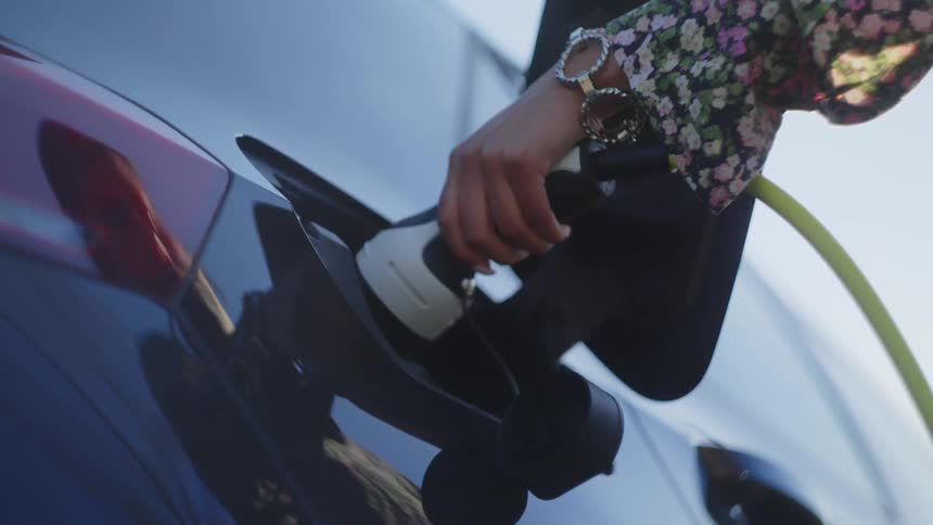 Woman plugs an electric car charger in to her automobile