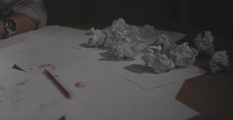 Man tosses a paper ball onto a pile of paper balls on a desk