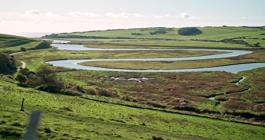 Winding river in the country with trees and plants on grass covered hills