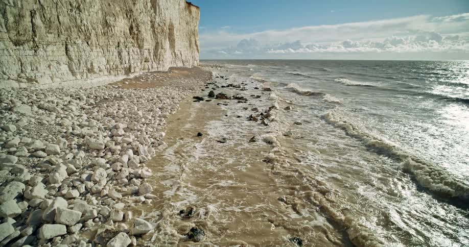 Waves crash against white cliffs under a sunny sky