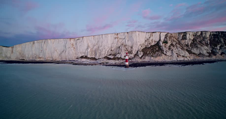 Aerial shot of a lighthouse at the beach of the coastal white cliff at sunset