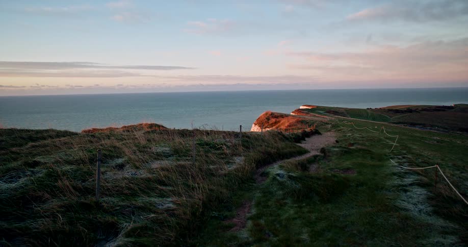Coastal trail on a green cliff overlooking the sea at sunset