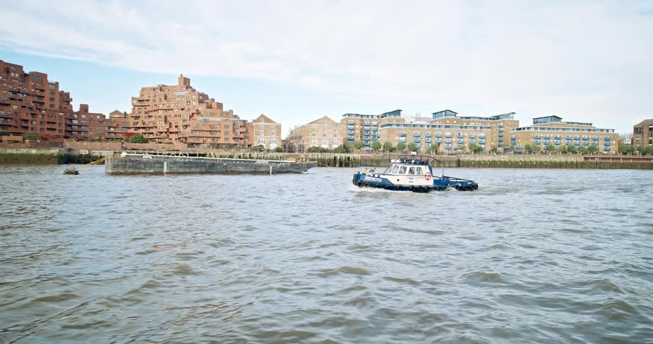 A tugboat travels along the thames river near some apartment buildings