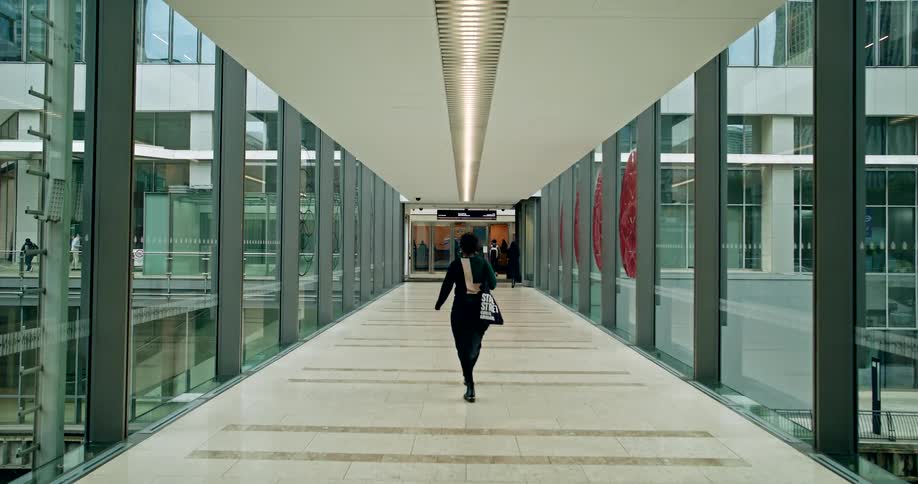 A woman walks down a long glass enclosed walkway in a modern building