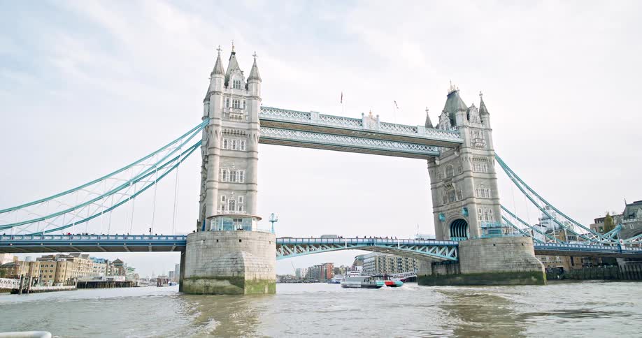 Boat sails under the tower bridge in london as traffic and pedestrians move on the bridge
