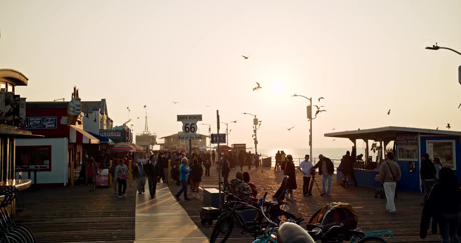 People walk near buildings and concession stands on the coast as a flock of seagulls fly overhead