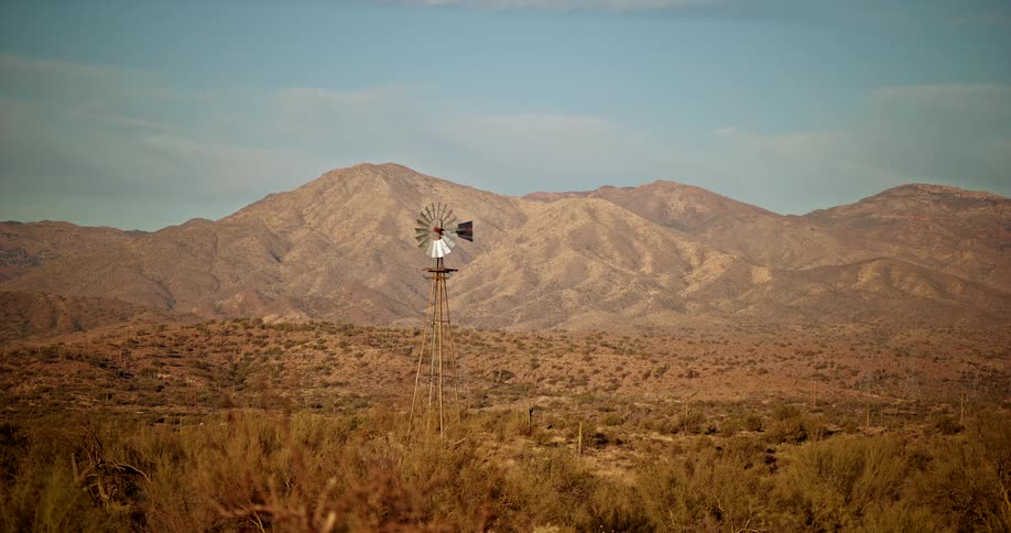 Metal windmill standing alone in an arid landscape with mountains in the background
