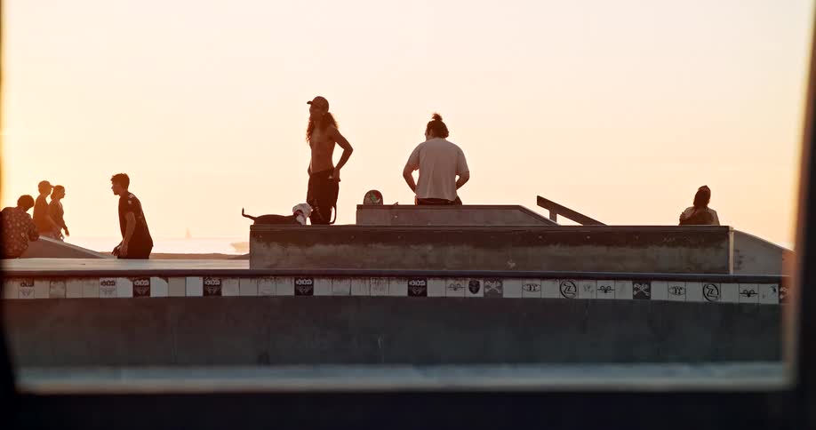 Small group of young people hanging out and skateboarding in an urban area outdoors during sunset