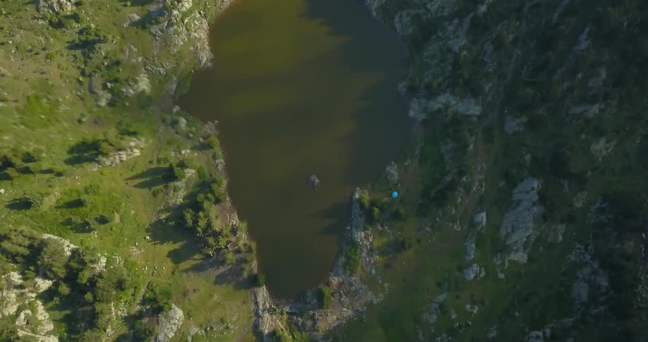 A pond is surrounded by mountains and green