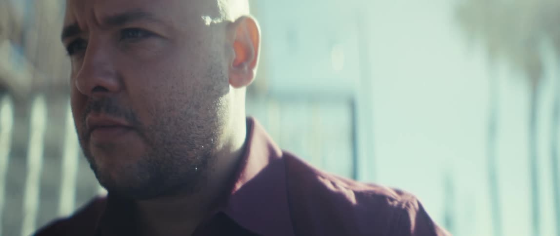 A bald man with a serious expression looking thoughtfully into the distance on a sunny day