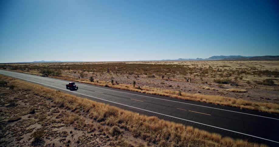 Aerial of a red truck driven on an empty road in a rural area during daytime