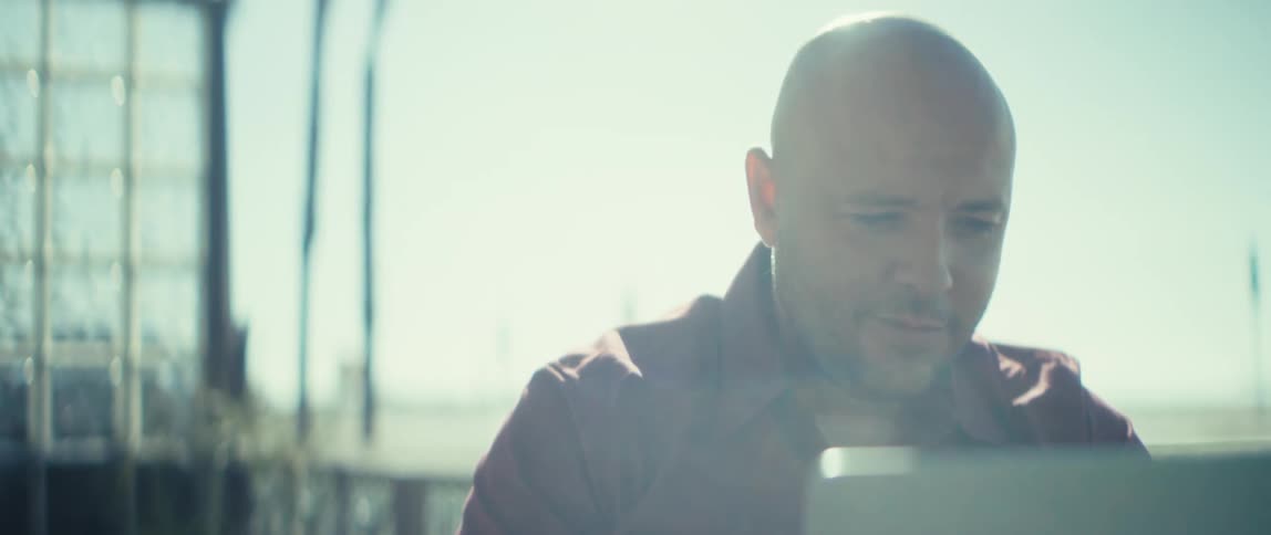 Close up of a man using a laptop computer while sitting at a table outdoors during daytime