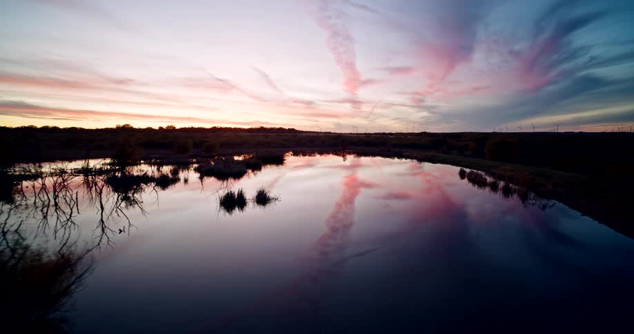 The sky above is reflected by the surface of a lake surrounded by shrubs