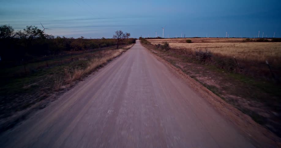 Dirt road surrounded by fields and wind turbines at dusk
