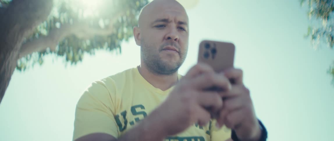 Man in a yellow shirt using a smartphone under bright sunlight