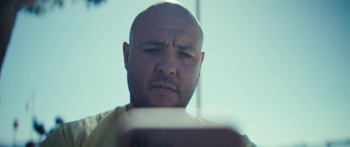 This video provides a very tight slightly lowangle closeup of the bald mans face as he looks intently down at a screen or phone held just out of focus in the foreground he has a serious slightly furrowed expression throughout the clip