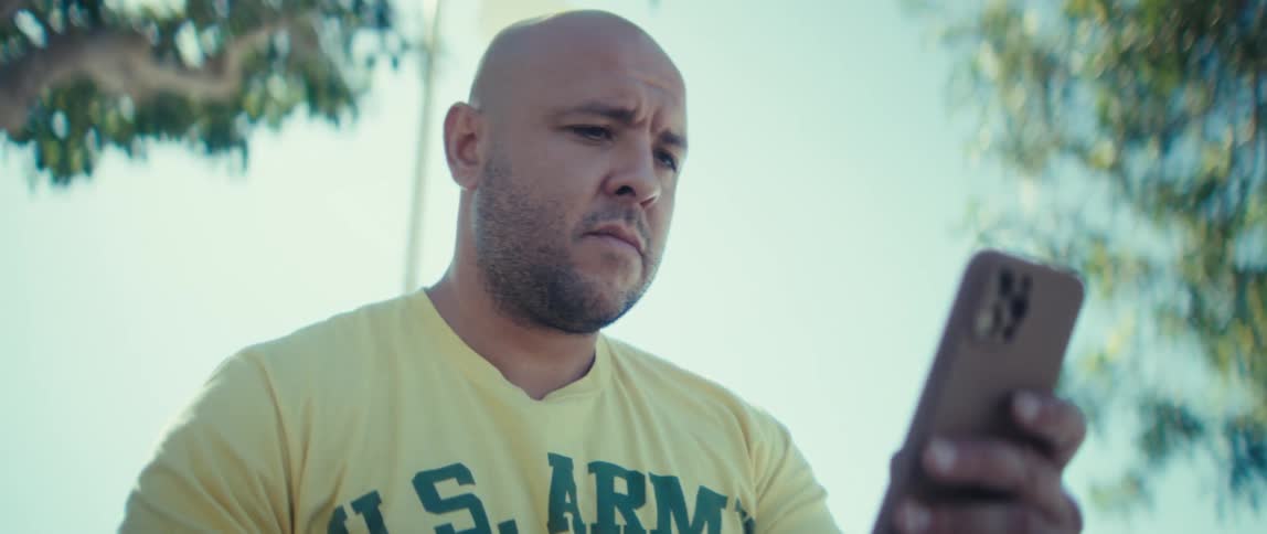 Man wearing a us army veteran t shirt focuses on his smartphone while sitting in a park