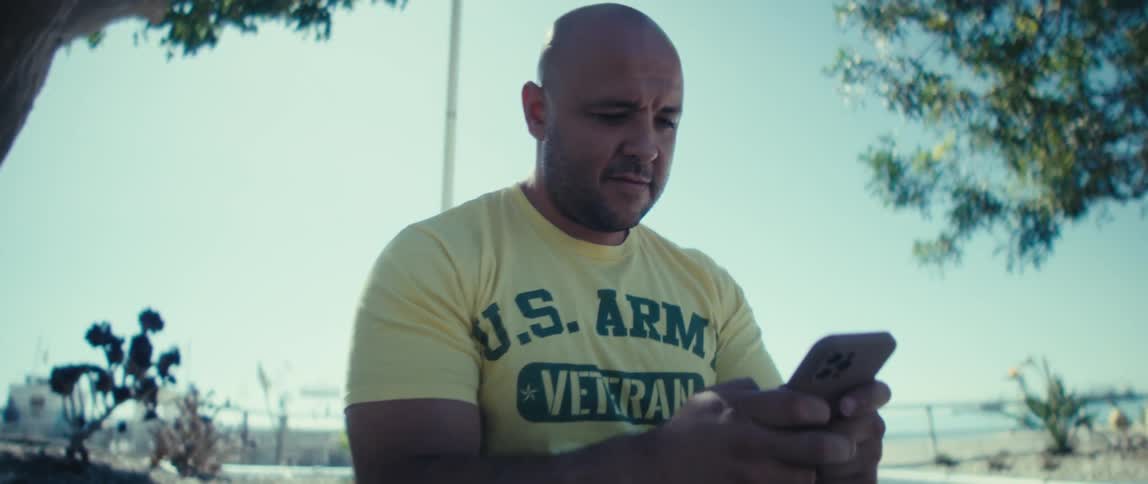 A man is sitting near a tree outside and looking at his cellphone