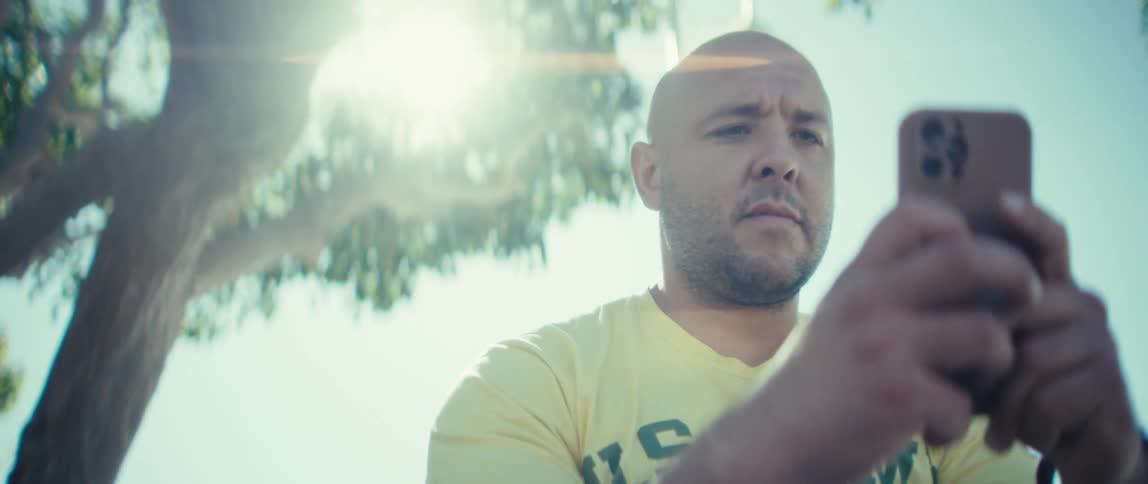 Man standing outside near a tree texting on his cell phone
