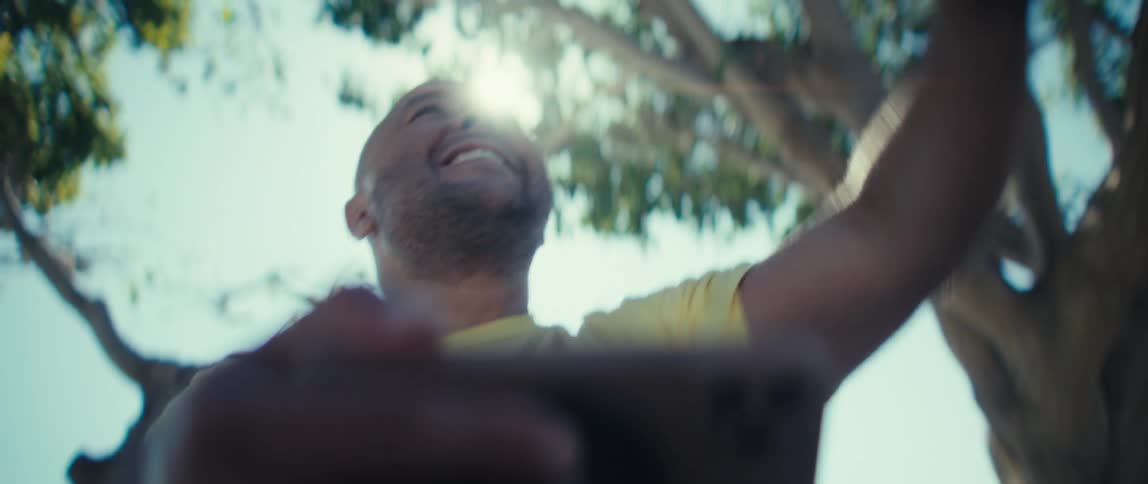A man watches a video on his smart phone smiling and shaking his fist in tense expectation then releases it in celebration with laughter and pumping his fist in the air