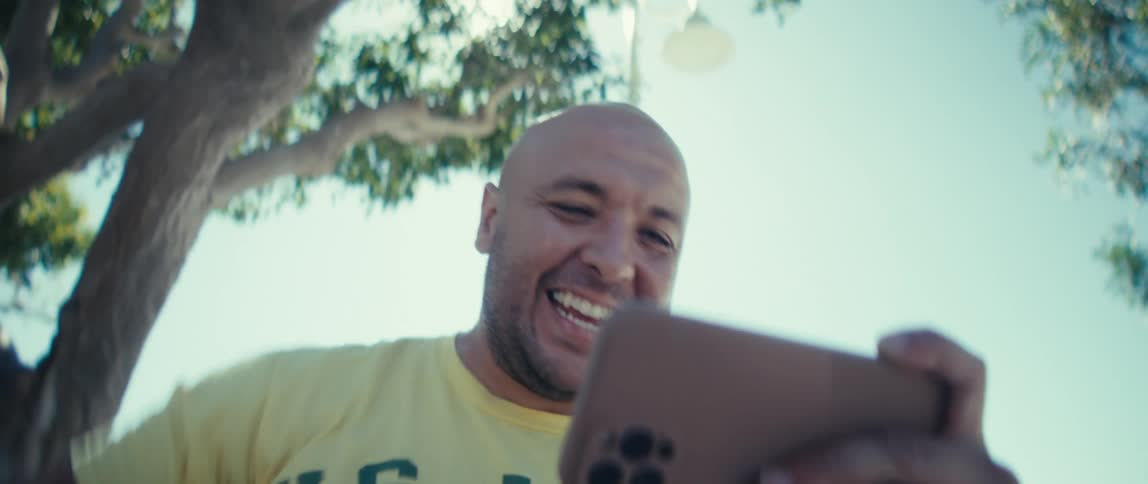 Man holds a phone smiling under the sunlight