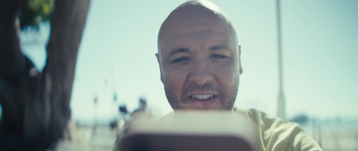 A man smiles and waves as he talks into a phone