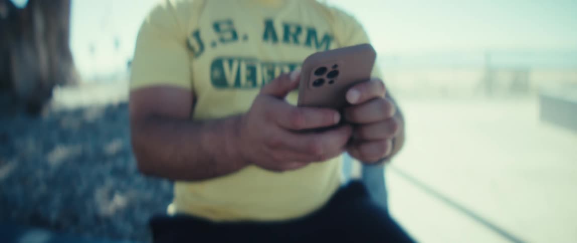 The clip begins with a focused shot on the mans face as he appears to be contemplating or reading something offscreen the camera pans down to reveal his shirt which is bright yellow with green text after a few seconds he lifts his smartphone into vi