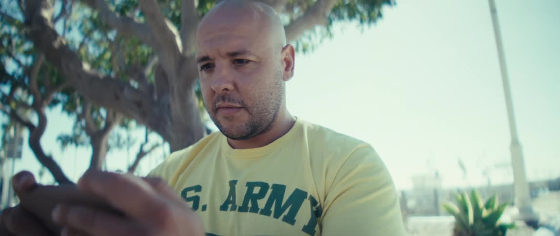 Man sitting near a tree on the coast looks at his phone and cheers raising his fist in celebration