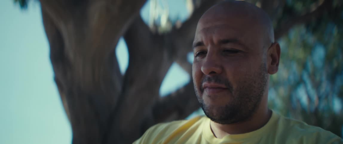 Man looking to the side while holding a phone under the shade of a tree