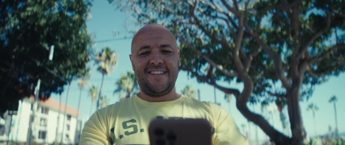 Man holding a phone while looking into the distance in a sunny location