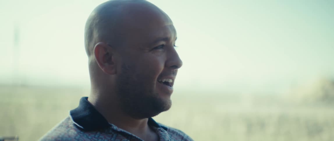 A bald man smiles as he carries on a conversation while outdoors