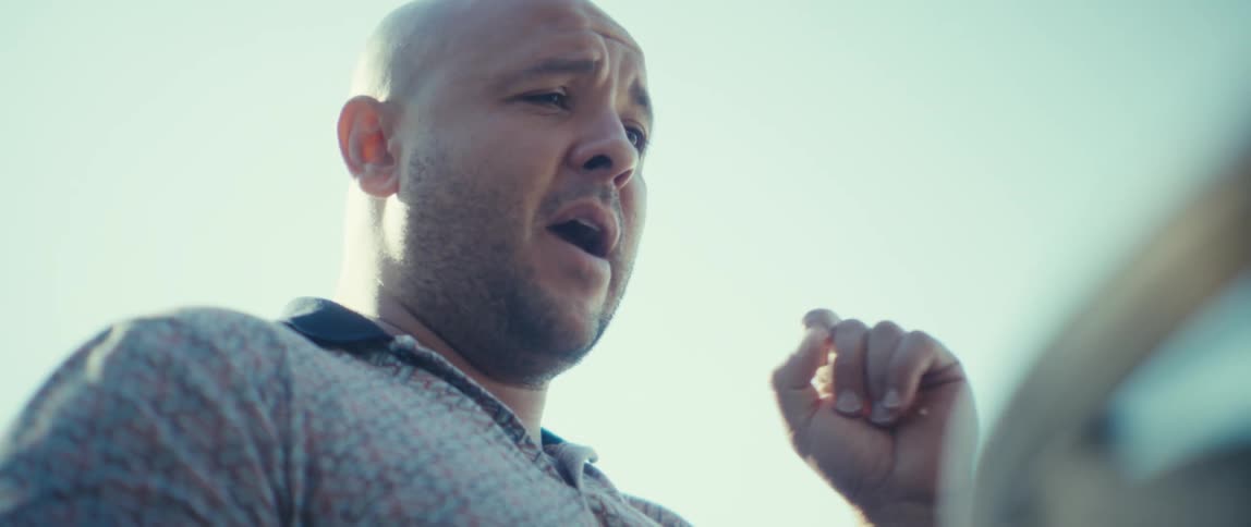 Young bald man wearing a polo shirt talking and gesticulating outdoors during day time