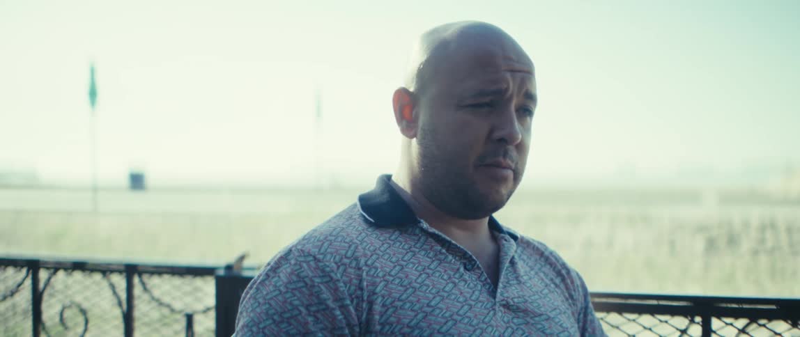 Close up of a man speaking on a call while sitting at an outdoor table during daytime