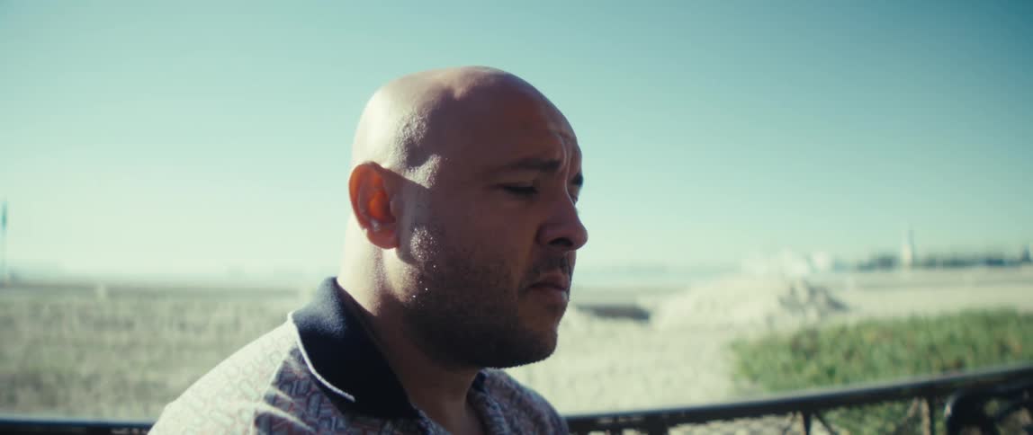 Man typing on a laptop at an outdoor table overlooking the sea