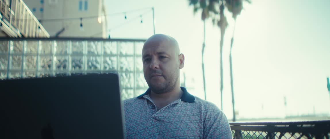 Man sitting at a table on a patio on the coast having a conversation on a laptop computer